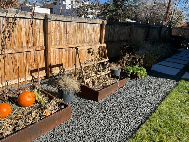 A backyard with a wooden fence , planters , pumpkins and a ladder.