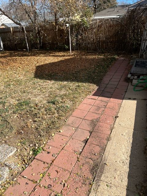 A brick walkway leading to a yard with a house in the background.