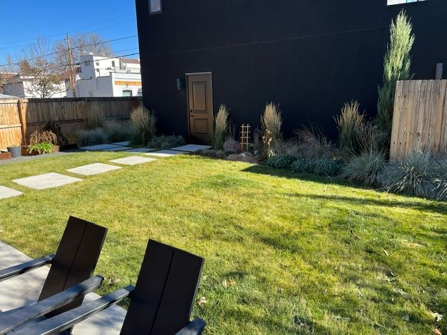 There are two chairs in the grass in the backyard of a house.