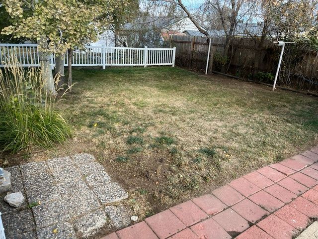 A backyard with a white fence and a brick walkway.