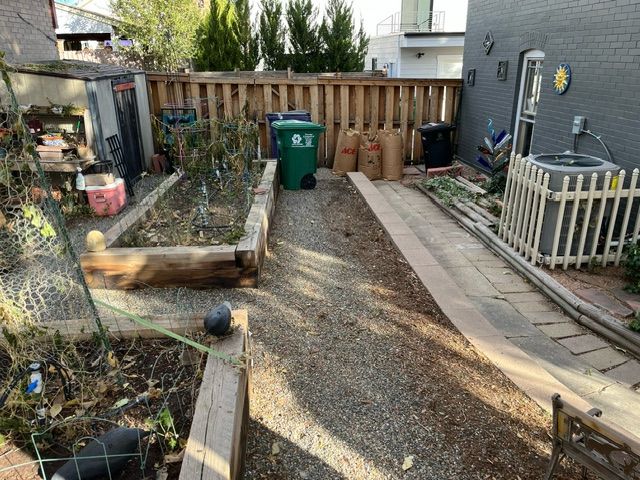 A backyard with a wooden fence and a green trash can.
