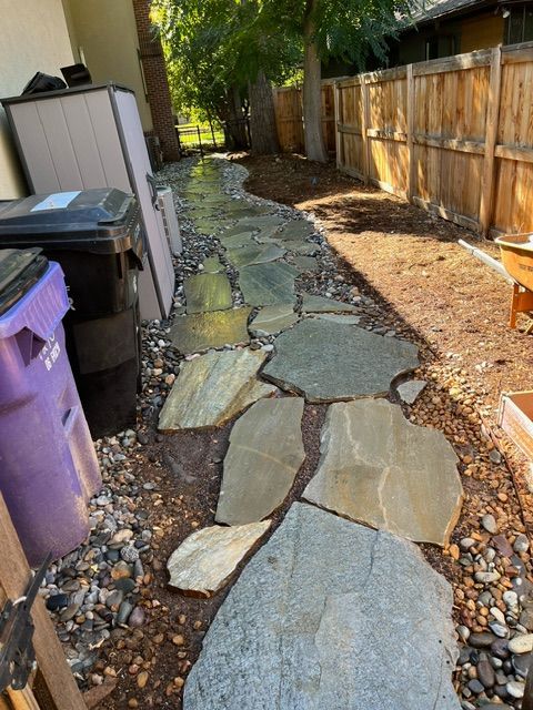 A stone walkway in a backyard next to a wooden fence.
