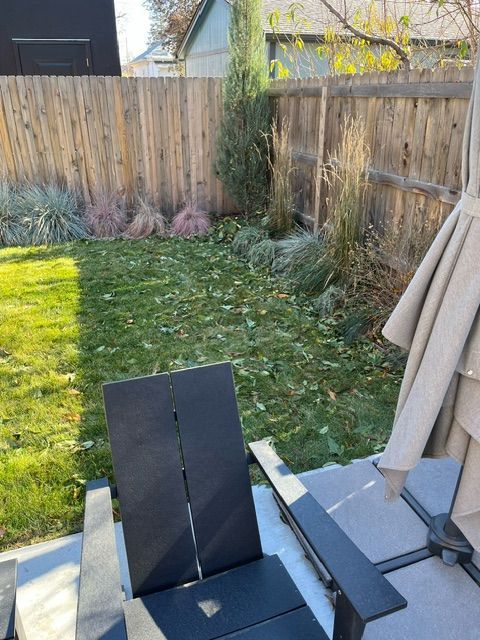A backyard with a wooden fence and chairs and umbrellas.