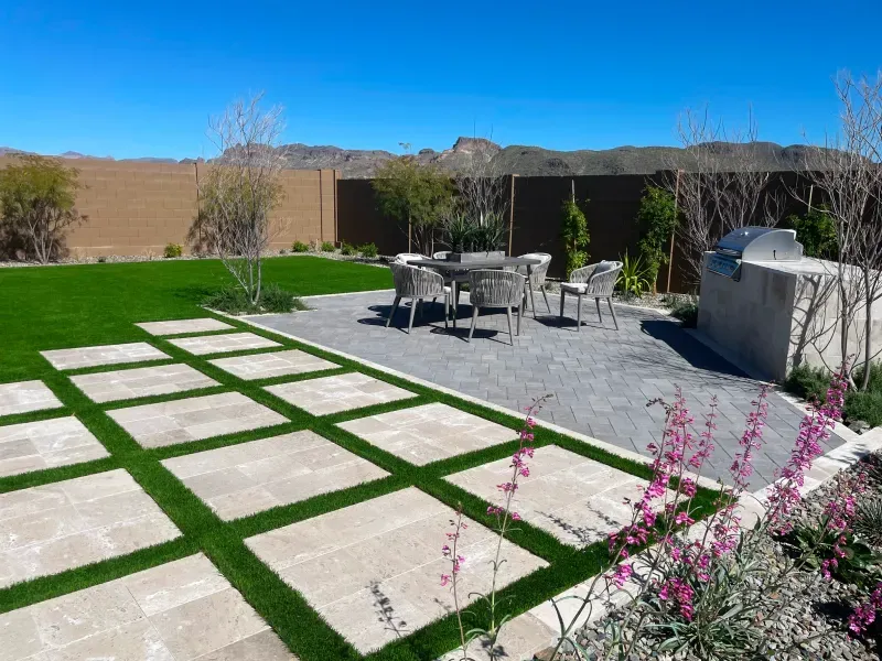 Backyard with a patio, lawn, seating, and built-in grill, set against a mountain backdrop.