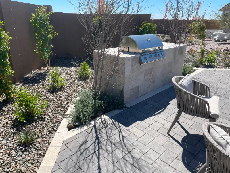 Outdoor patio with built-in grill on a stone structure, surrounded by greenery and seating.