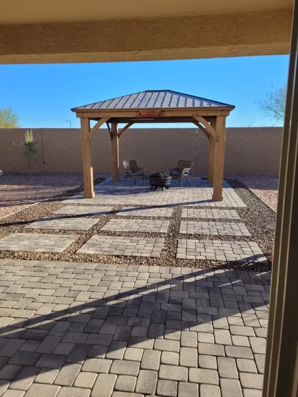 Backyard with a gazebo, stone patio, and a small dog on a sunny day.