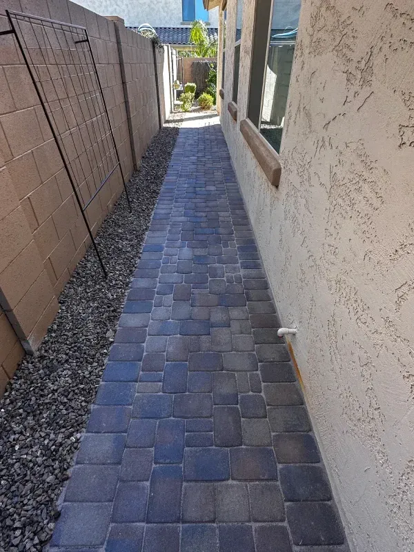Brick walkway alongside a textured beige wall and a dark gray cinder block fence.