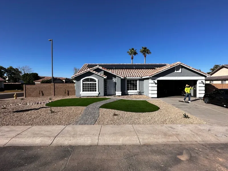 Gray house with solar panels on roof, green lawn, gravel landscaping, and worker.