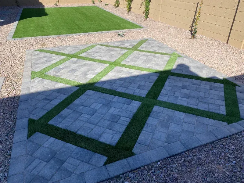 Paver patio with green turf design, surrounded by gravel. A green turf rectangle is in the background.