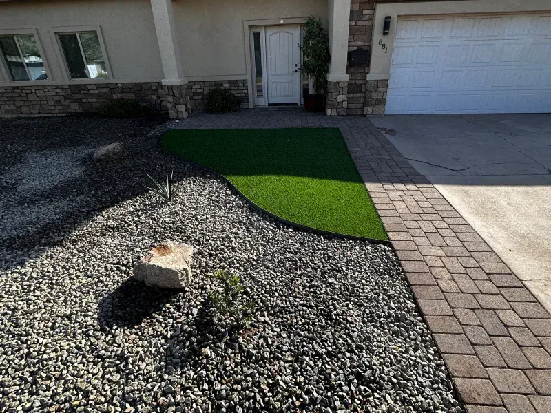 Front yard with artificial turf, rock landscaping, and a brick walkway leading to the front door.