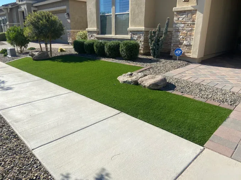 Front yard with artificial turf, walkway, and landscaping in front of a beige house.