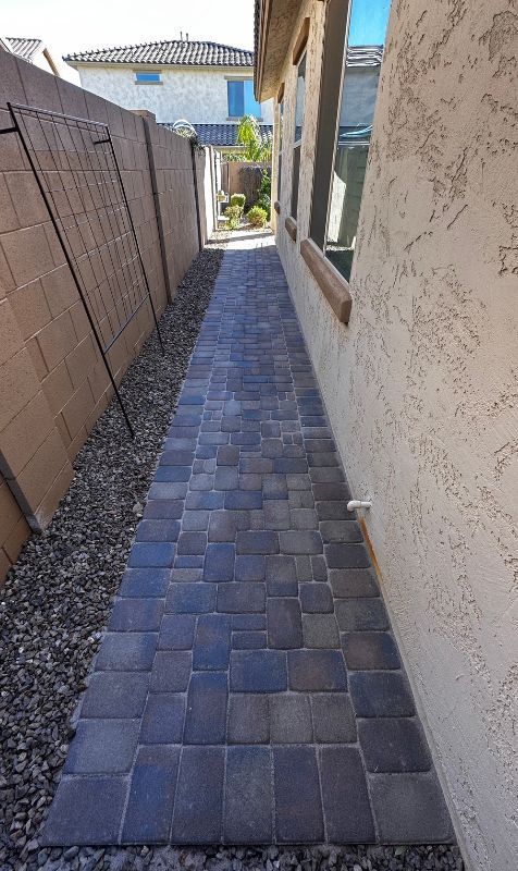 Narrow brick walkway between a beige stucco house and a stone wall, with a gravel border.