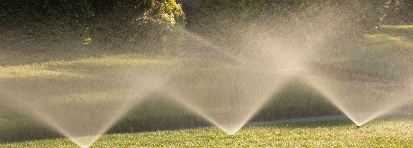 Sprinklers watering a green lawn, spraying water in a zigzag pattern.