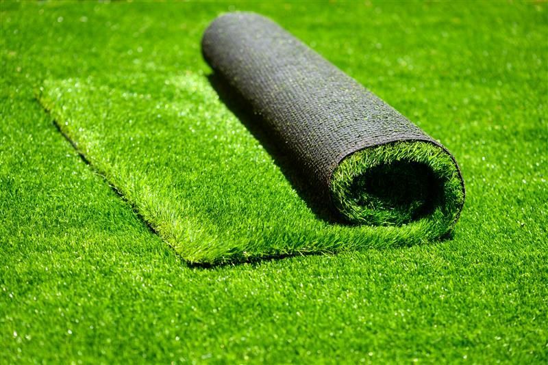 Roll of artificial turf unrolled on a green surface.