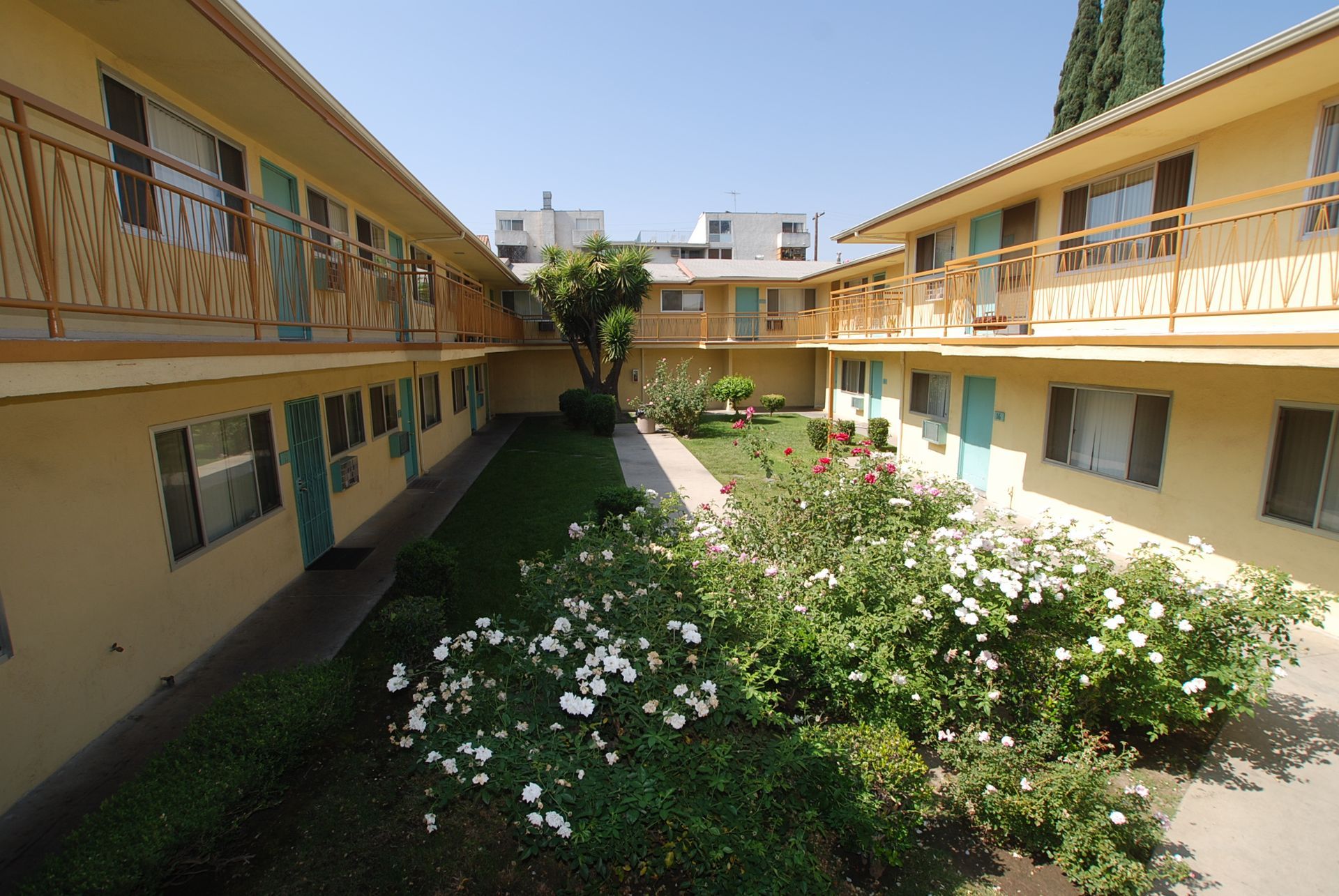 Courtyard apartment buildings with turquoise doors, tan walls, and a central garden with flowers.