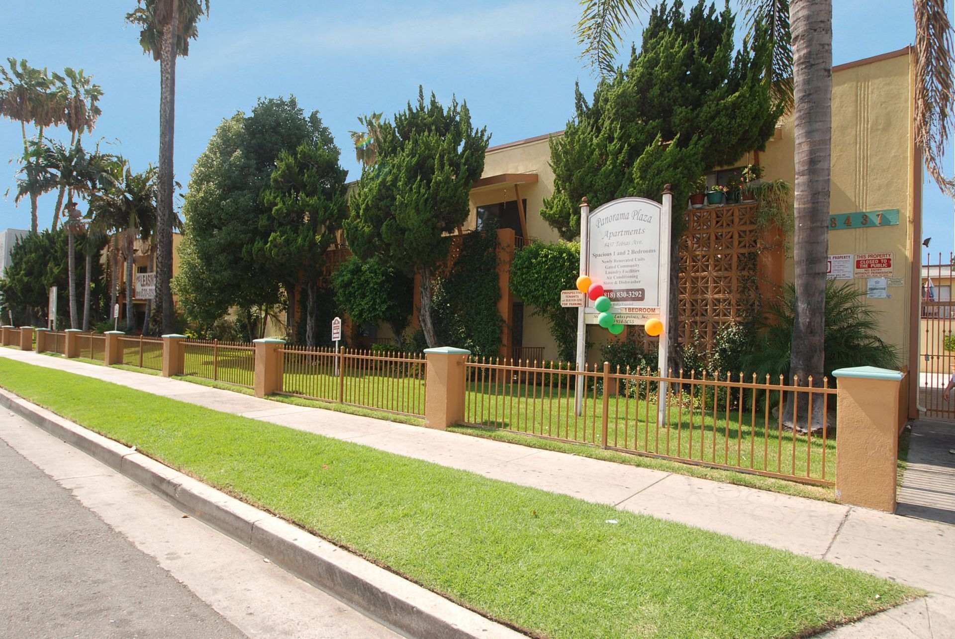 Yellow building with a small picket fence, lush green lawn, and sign; sunny day.