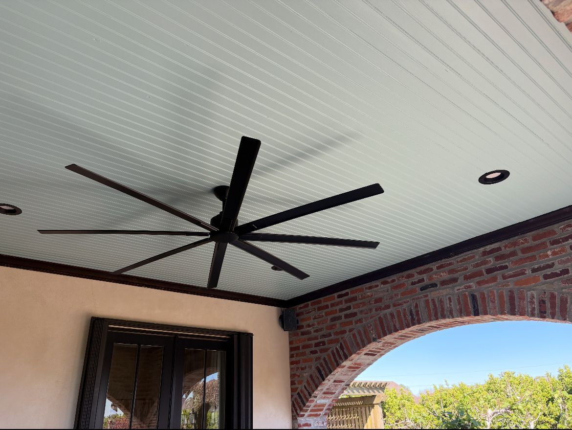 A large ceiling fan is hanging from the ceiling of a porch.