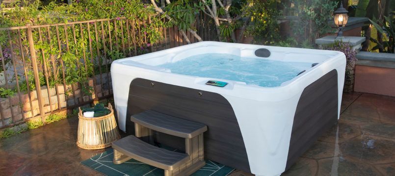 A hot tub is sitting on a patio next to a fence.