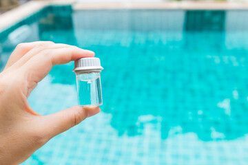 A person is holding a bottle of water in front of a swimming pool.