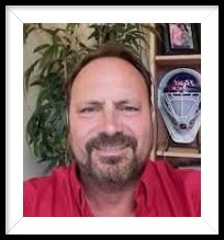 A man with a beard is wearing a red shirt and smiling for the camera.