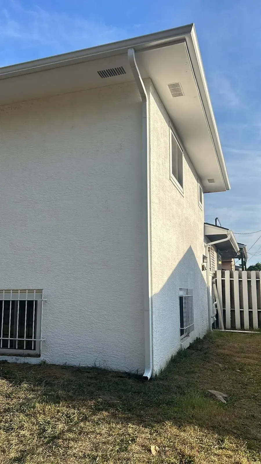 The side of a white house with a fence in the background.
