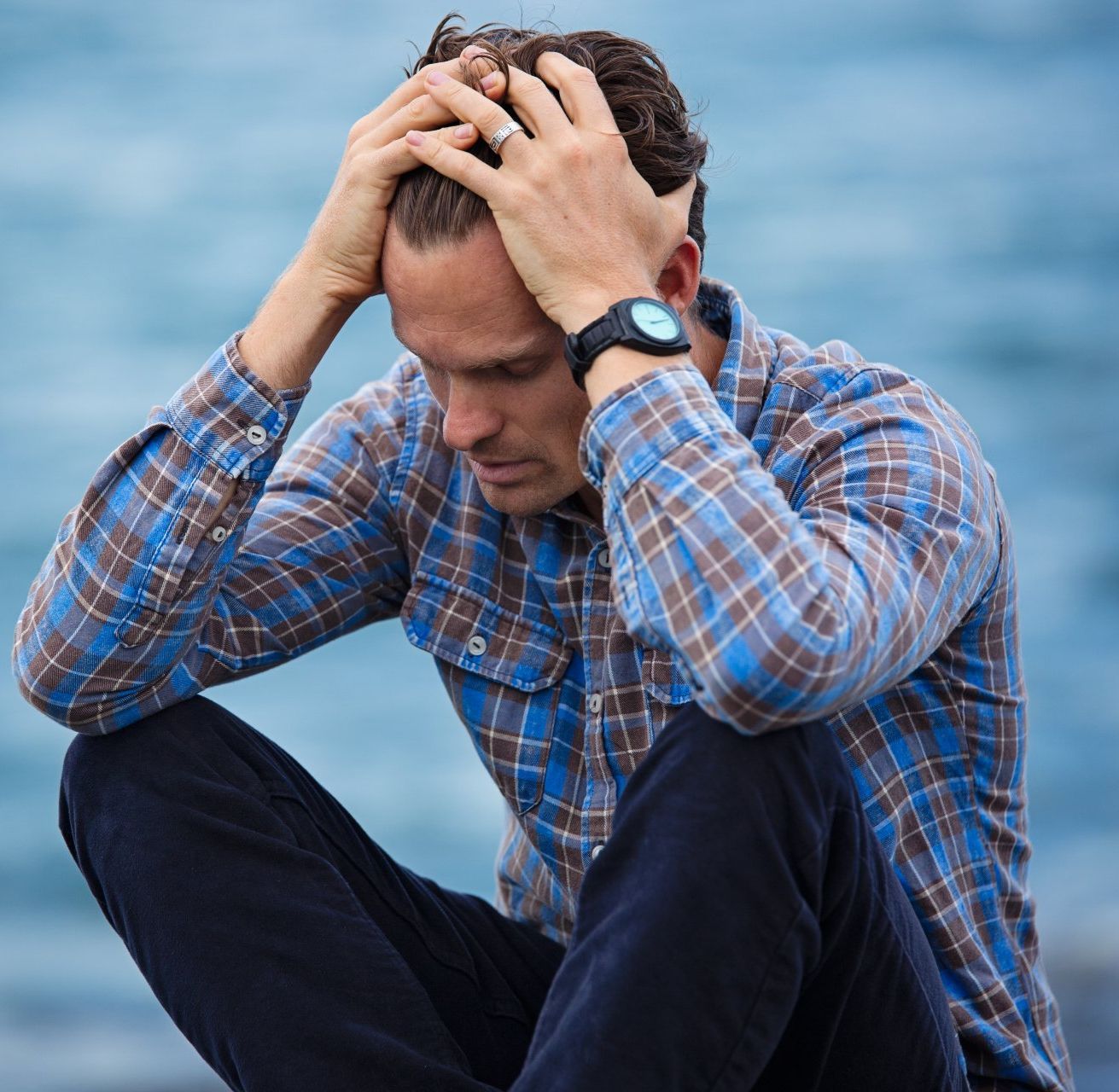 a depressed man in a plaid shirt is kneeling down with his hands on his head .