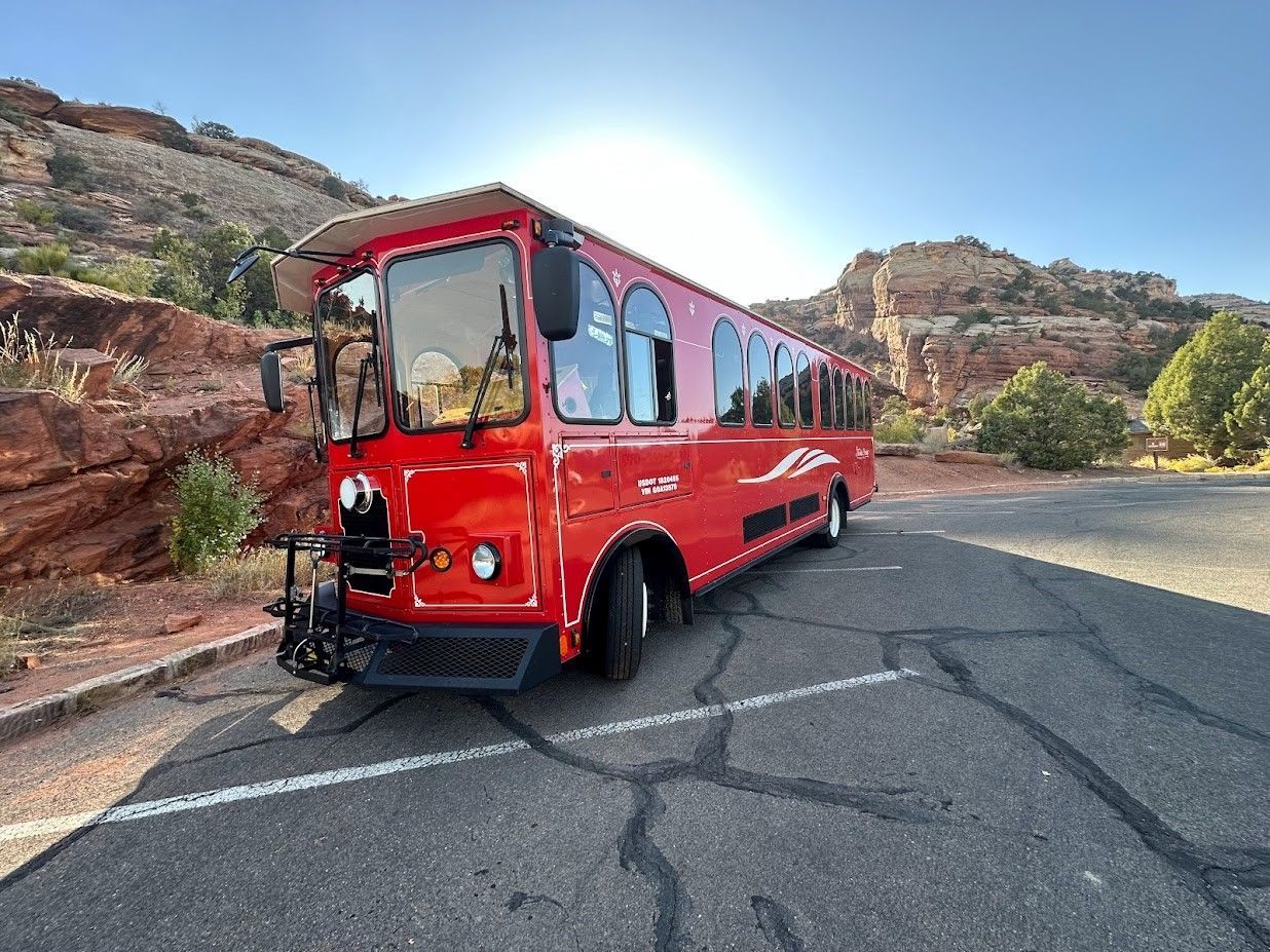 A red trolley bus is parked in a gravel lot.