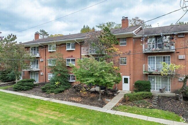 Red brick apartment building with balconies, trees, and a green lawn.