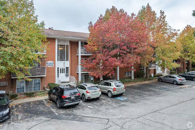 Apartment building with cars parked out front, trees with autumn foliage.