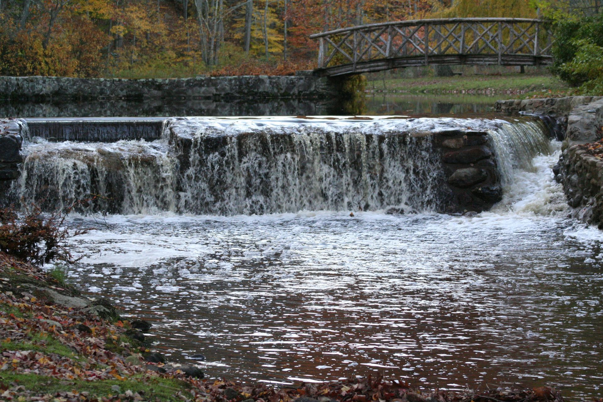 A small waterfall with a bridge in the background