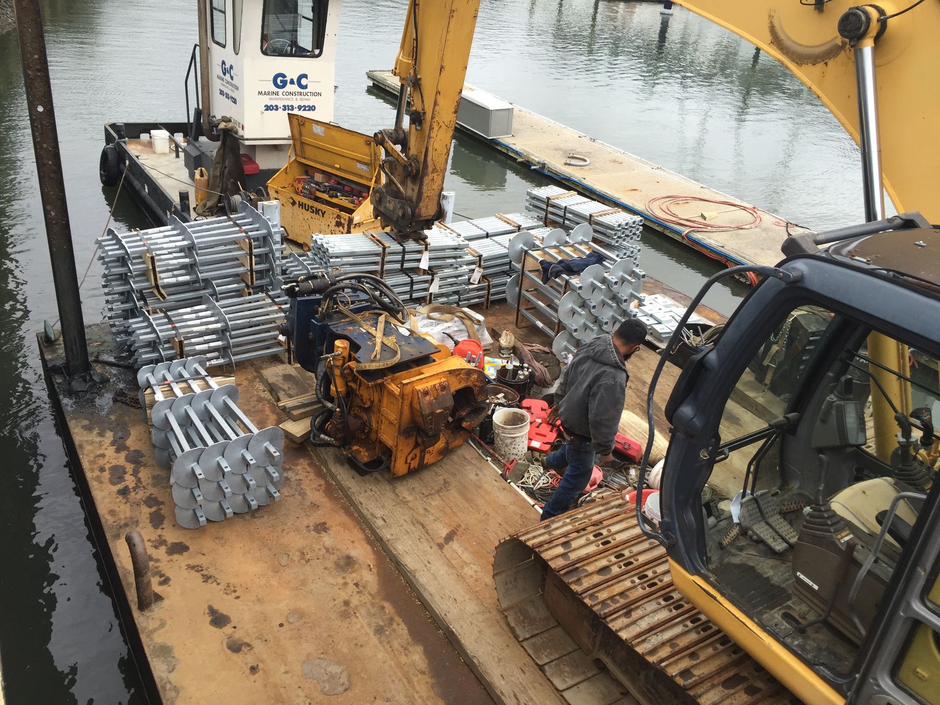 A man is standing next to a yellow excavator on a boat.