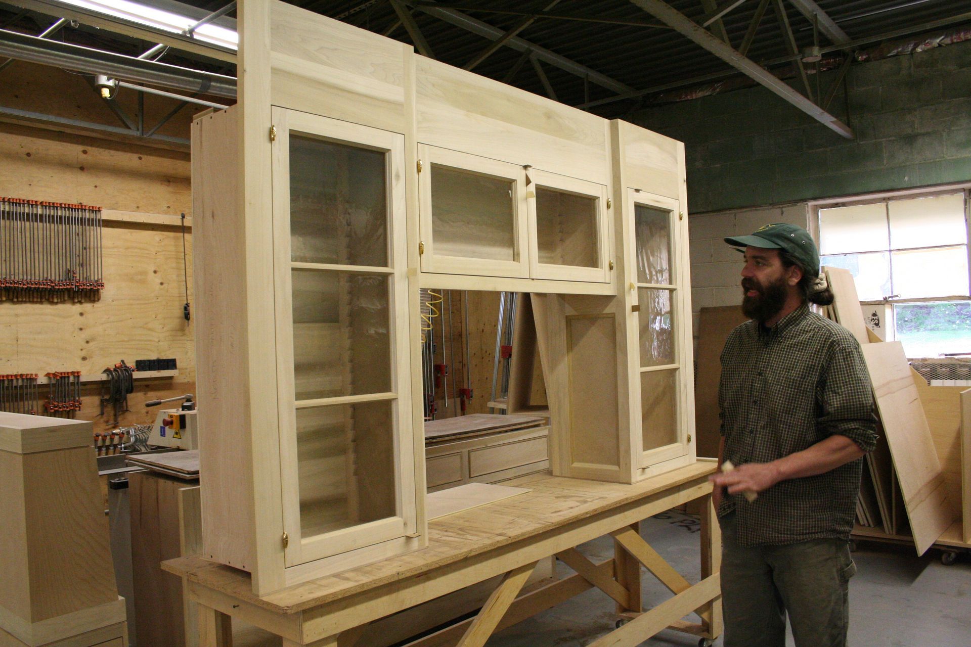 A man with a beard is standing next to a wooden cabinet in a workshop.