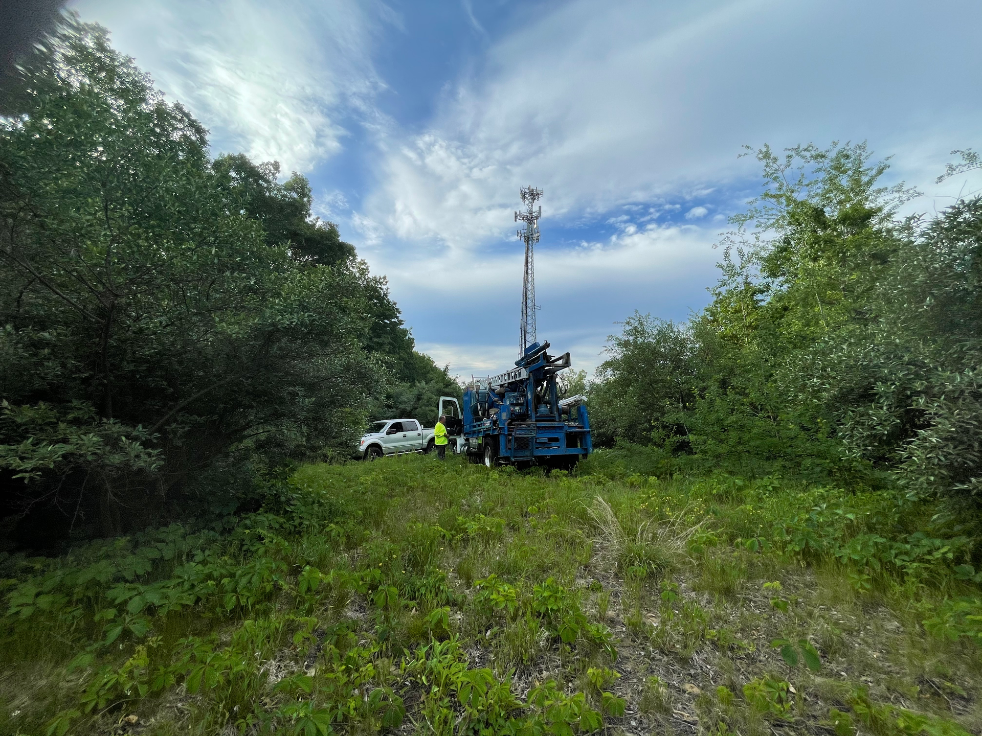 A group of people are standing in a field with a drill in the middle of it.