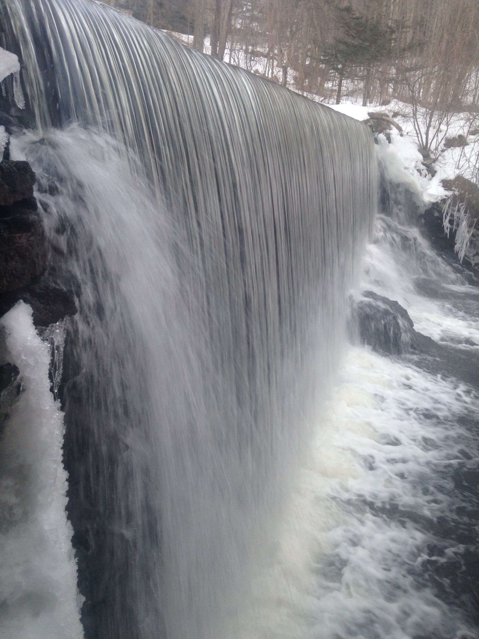 A waterfall is surrounded by snow and trees in the middle of a forest.