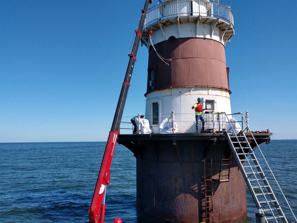 A man standing on top of a lighthouse next to a red crane