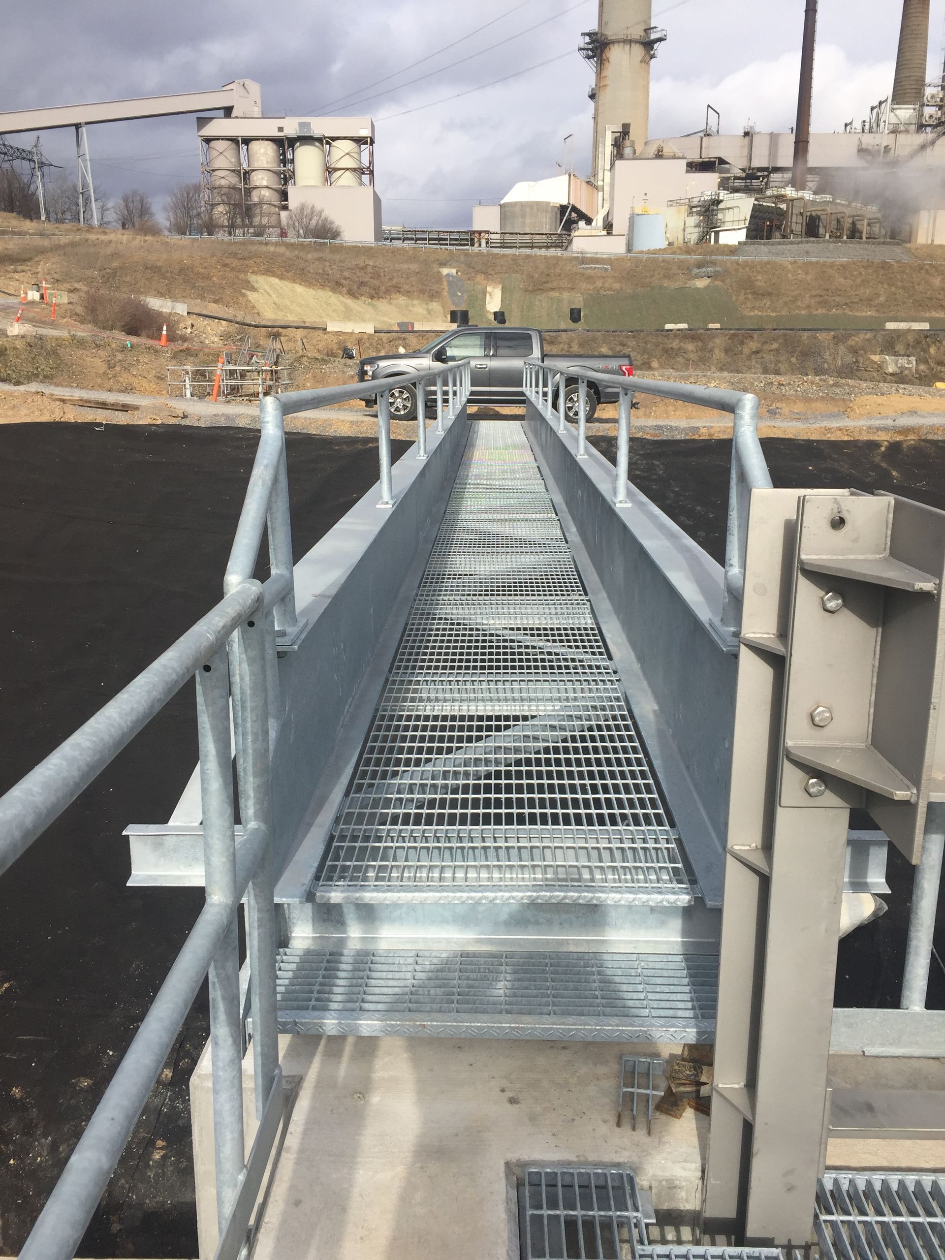A metal bridge with stairs leading to a factory in the background