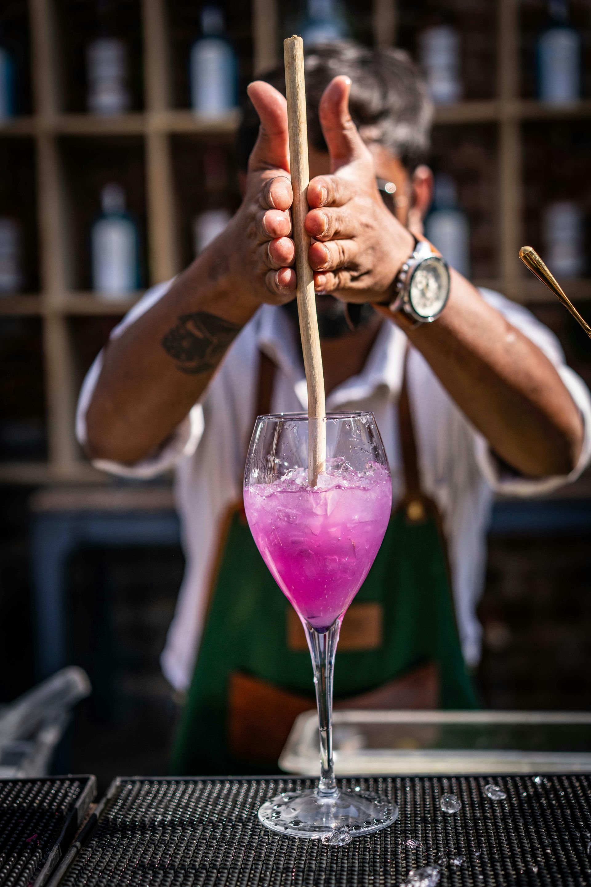 A bartender is stirring a pink cocktail with a wooden stick.