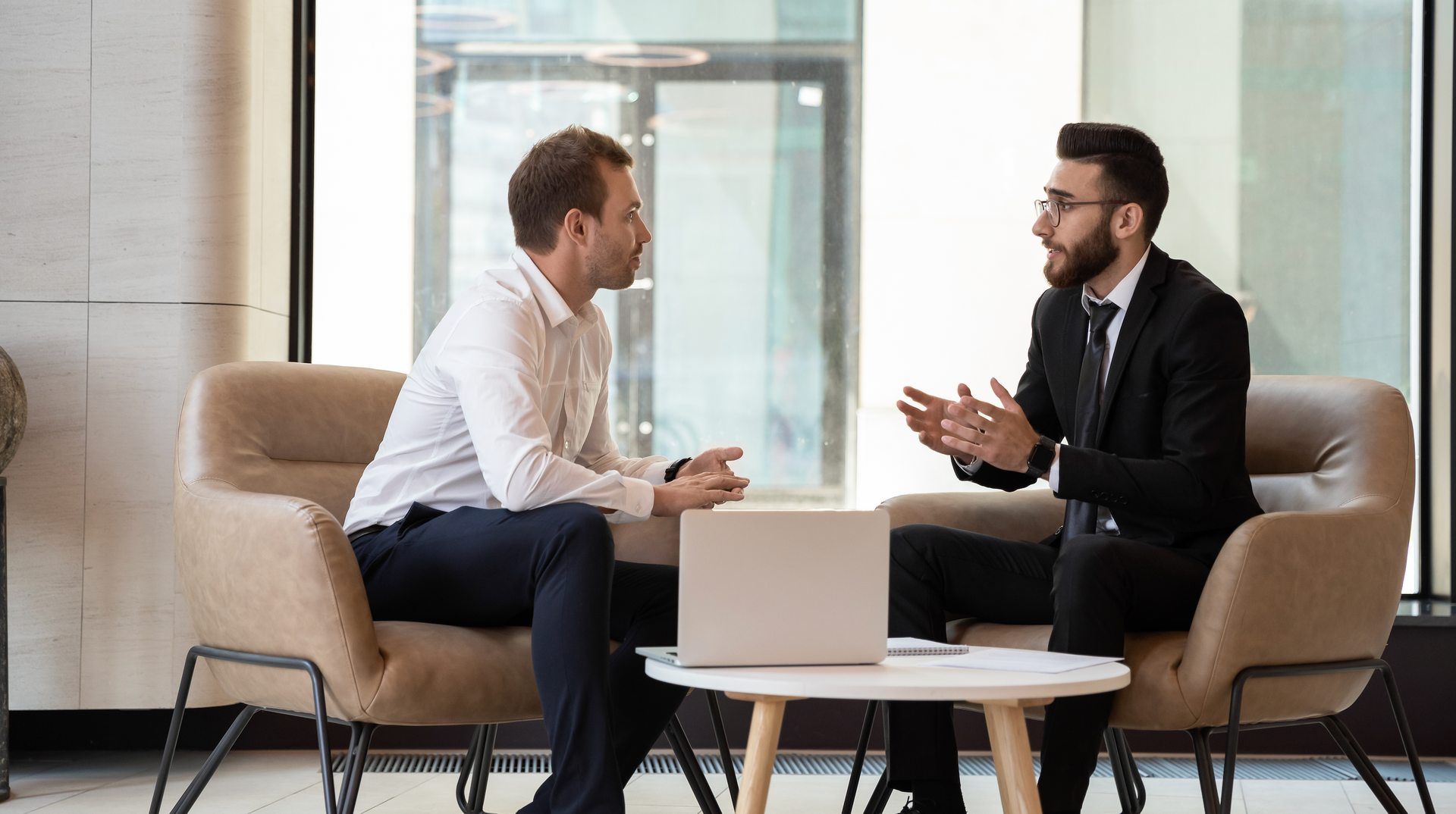 Two men are sitting on a couch and talking to each other.