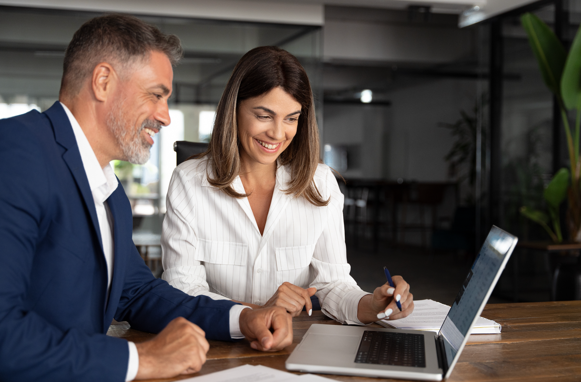 A man and a woman are sitting at a table looking at a laptop computer.
