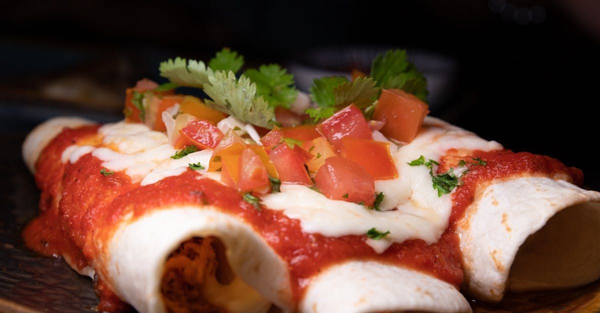 A close up of two enchiladas with tomato sauce and cheese on a wooden table.