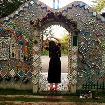 A woman standing in a stone archway holding her hands in a heart over her head.