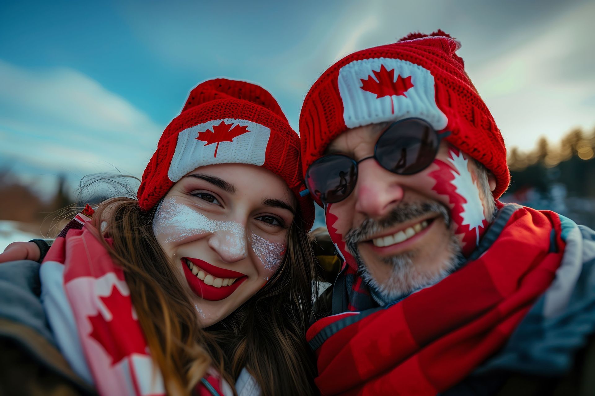 Two smiling individuals wearing red Canadian-themed hats and scarves, with face paint featuring the Canadian flag, standing outdoors in a rural setting during winter, representing community integration and pride associated with the Rural Community Immigration Class (RCIC).