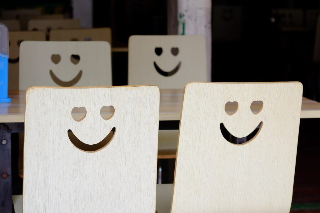 A set of four chairs at a table. The chairs have heart eyes and a smile as holes in the back.