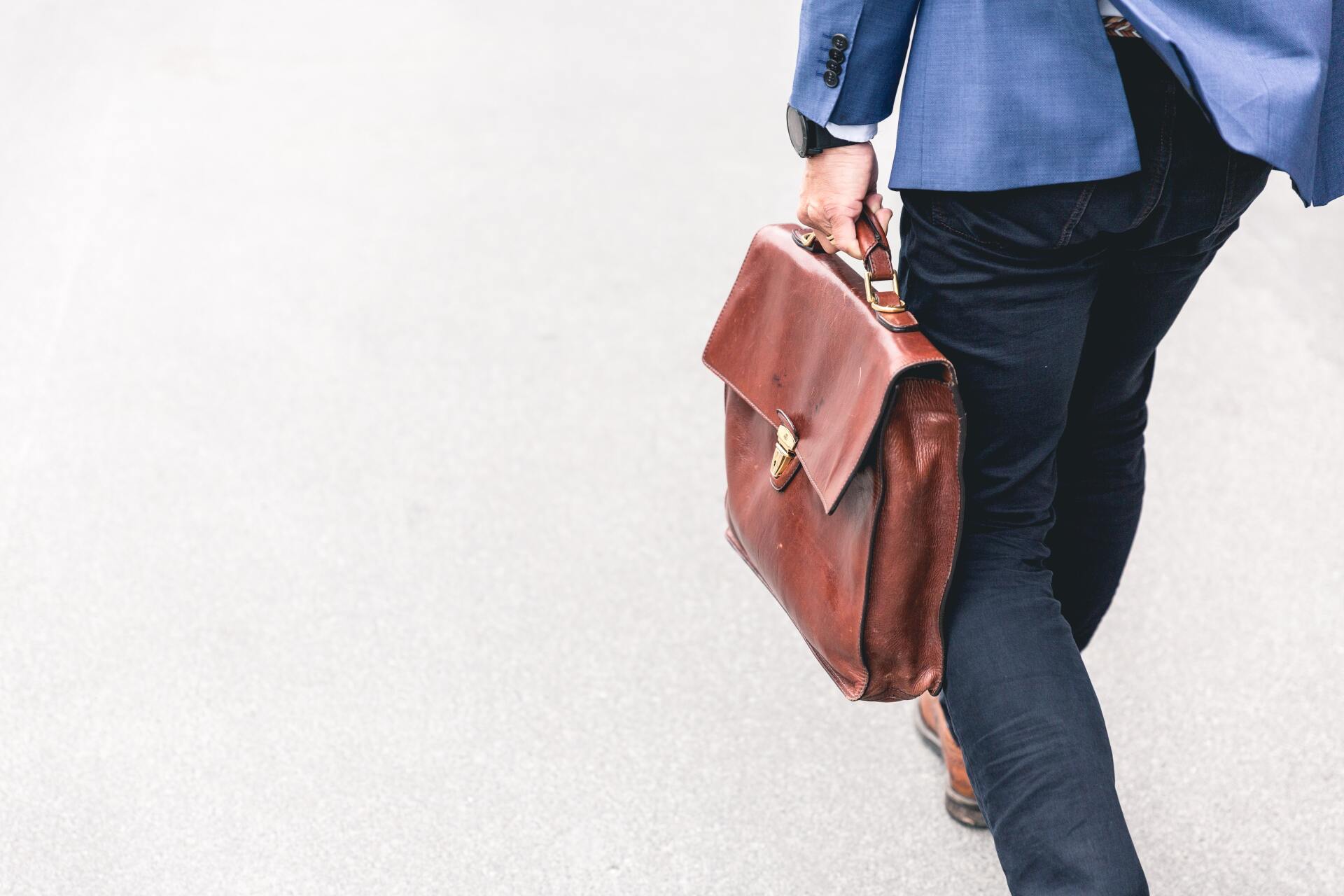 man walking while holding a soft, brown leather briefcase