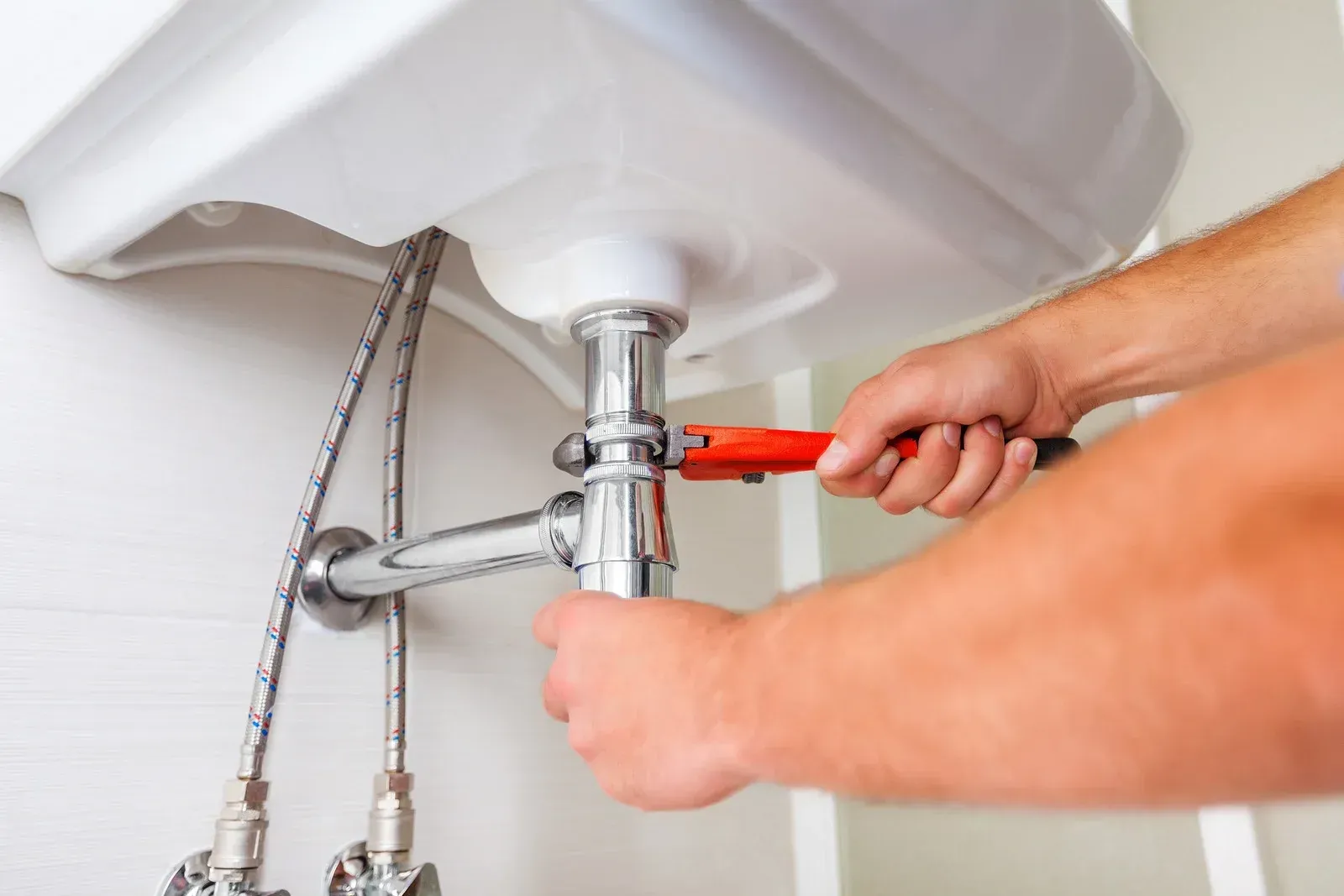Plumber tightening a bathroom sink pipe under a white basin with a wrench