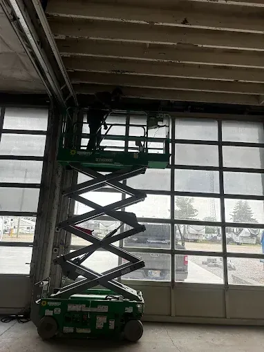 A man is standing on a scissor lift in a garage.