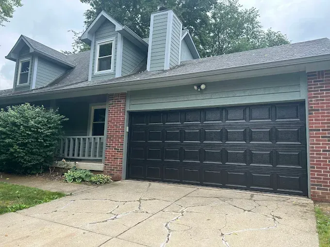 A house with a black garage door and a brick wall.