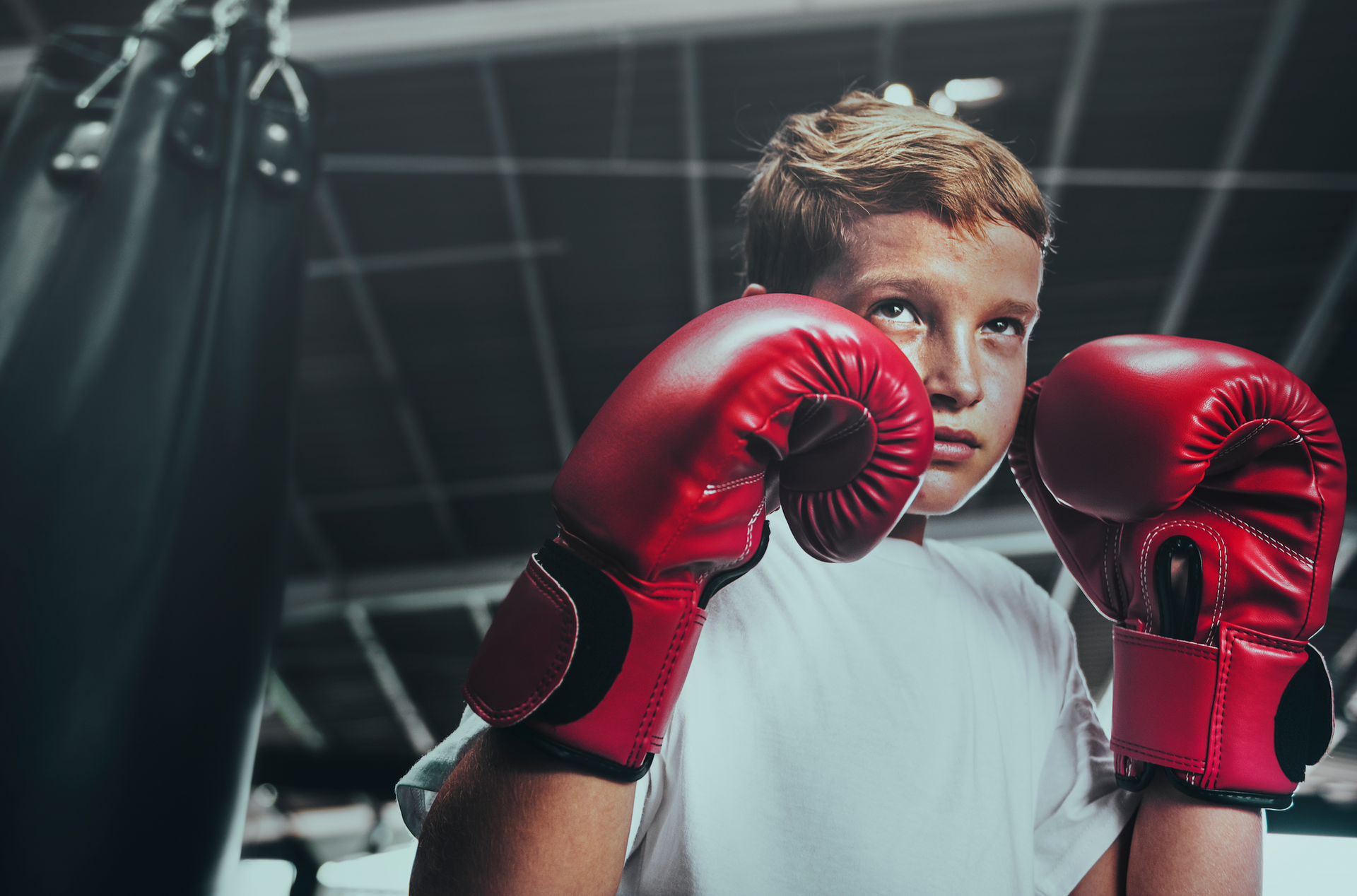 A young boy wearing red boxing gloves in a gym.