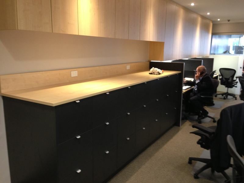 A Man Sits at A Desk in An Office Talking on A Cell Phone — Burns Custom Kitchens in Newcastle, NSW