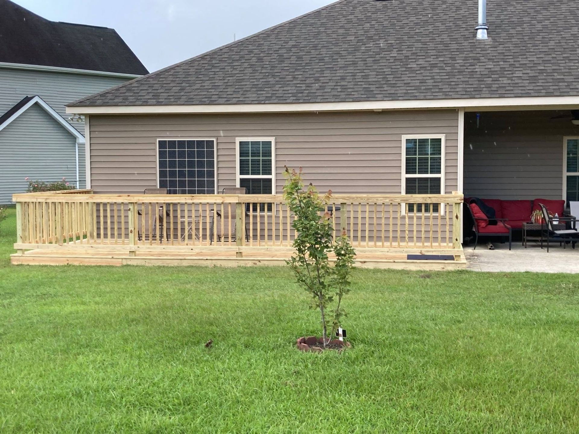 House with a wooden deck and a small tree in a grassy front yard